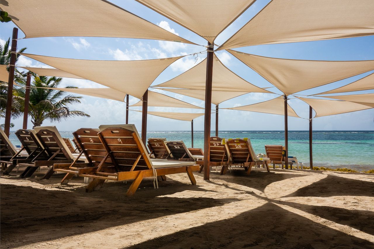 A serene beach scene featuring sun loungers under stylish shade sails by clear blue water.